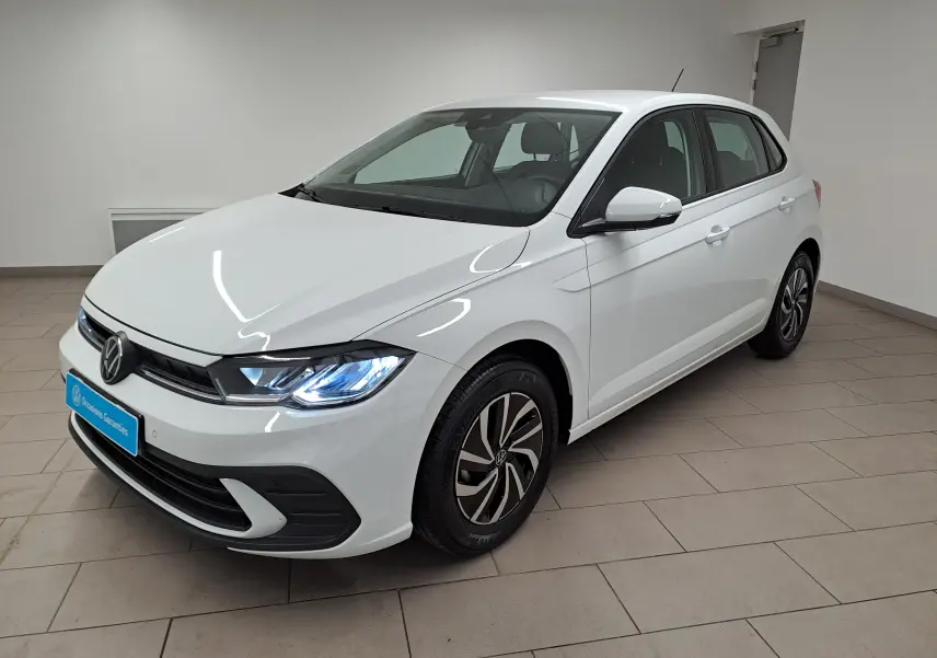 Volkswagen Polo blanc pur vue 3/4 avant droit, phares allumés et jantes au design distinctif en intérieur neutre.