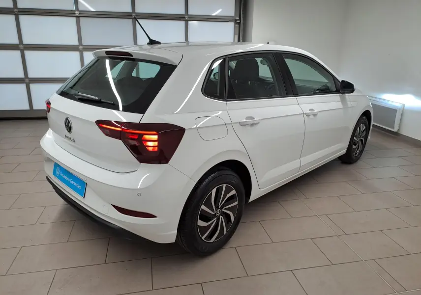 Vue 3/4 arrière droite d'une Volkswagen Polo blanche 2024 avec feux arrière allumés et jantes au design moderne.