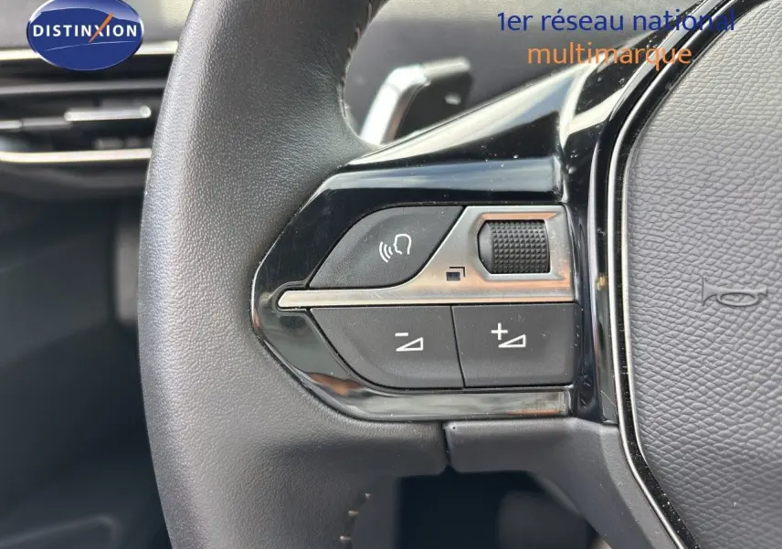 Gros plan sur les commandes gauche du volant noir du Peugeot 3008 Hybrid 180ch 2024, avec boutons de volume et fonction mains libres.