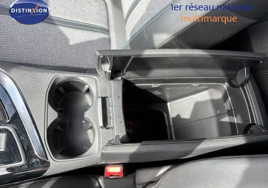 Vue plongeante sur la console centrale noire du Peugeot 3008 Hybrid 2024, avec accoudoir ouvert et porte-gobelets visibles.