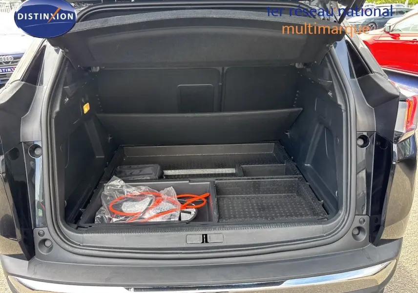 Coffre ouvert vu de l'arrière d'un Peugeot 3008 noir métal 2024 avec câble de recharge visible dans le compartiment.