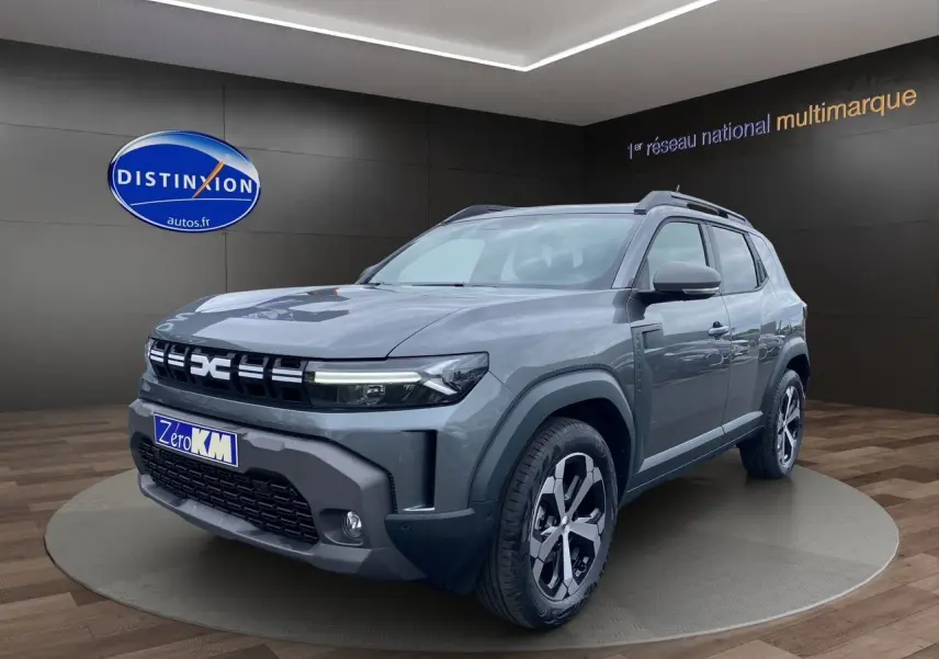 Vue 3/4 avant d'un Dacia Duster gris schiste hybride 2025 avec jantes noires et grises, sur podium showroom.