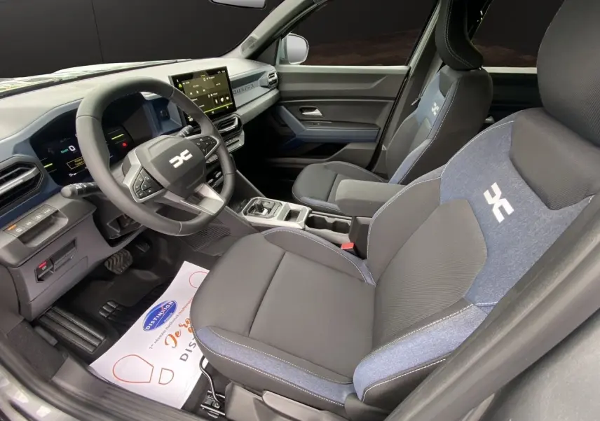 Vue intérieure côté conducteur du Dacia Duster hybride 2025 avec sièges noirs et bleus et tableau de bord numérique.