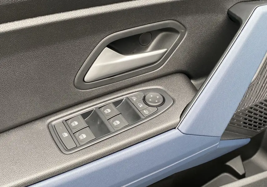 Détail de la porte côté conducteur du Dacia Duster 2025 hybride, avec habillage noir et bleu et commandes de vitres électriques.
