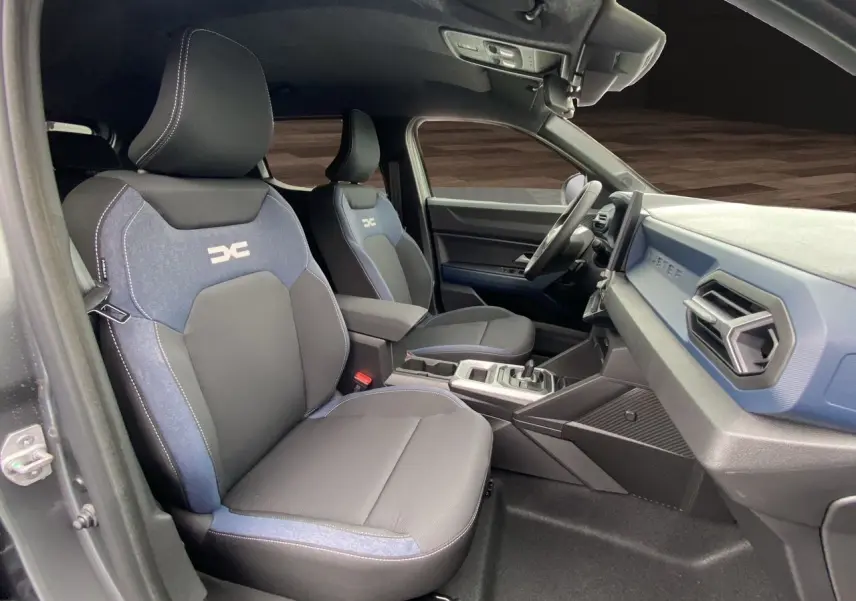Intérieur du Dacia Duster hybride 2025 montrant les sièges avant bleu et noir et le tableau de bord côté droit.