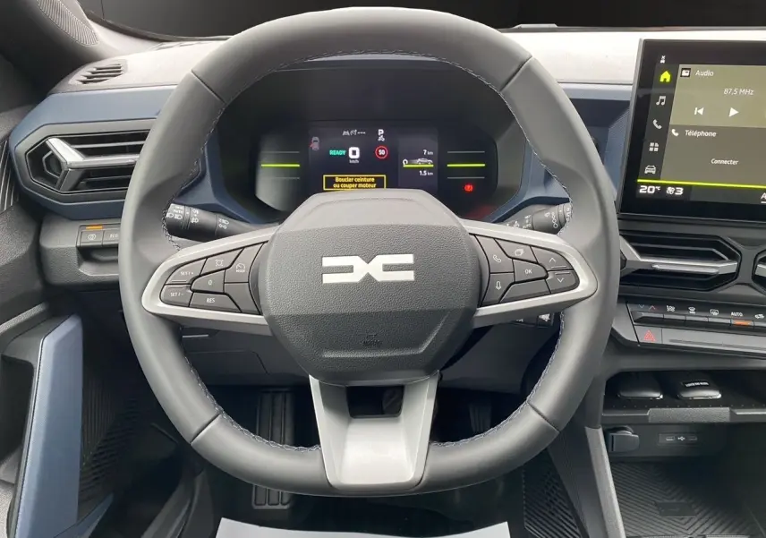 Vue rapprochée du volant et tableau de bord numérique du Dacia Duster hybride 2025 avec écran tactile et commandes intégrées.