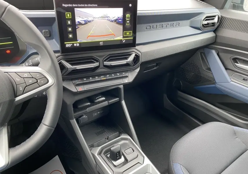Vue intérieure côté passager du tableau de bord gris bleu du Dacia Duster hybride 2025 avec écran multimédia et volant noir.