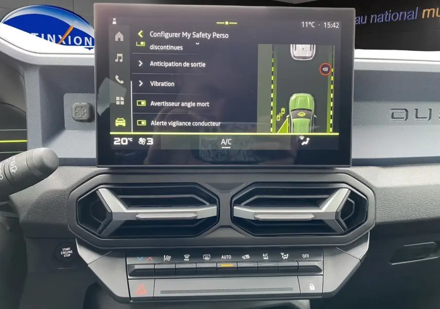 Tableau de bord noir-bleu du Dacia Duster 2025 avec écran tactile affichant les aides à la conduite et aérateurs hexagonaux.