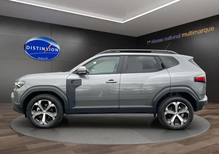 Profil droit du Dacia Duster 2025 gris schiste hybride avec jantes alliage et barres de toit noires.