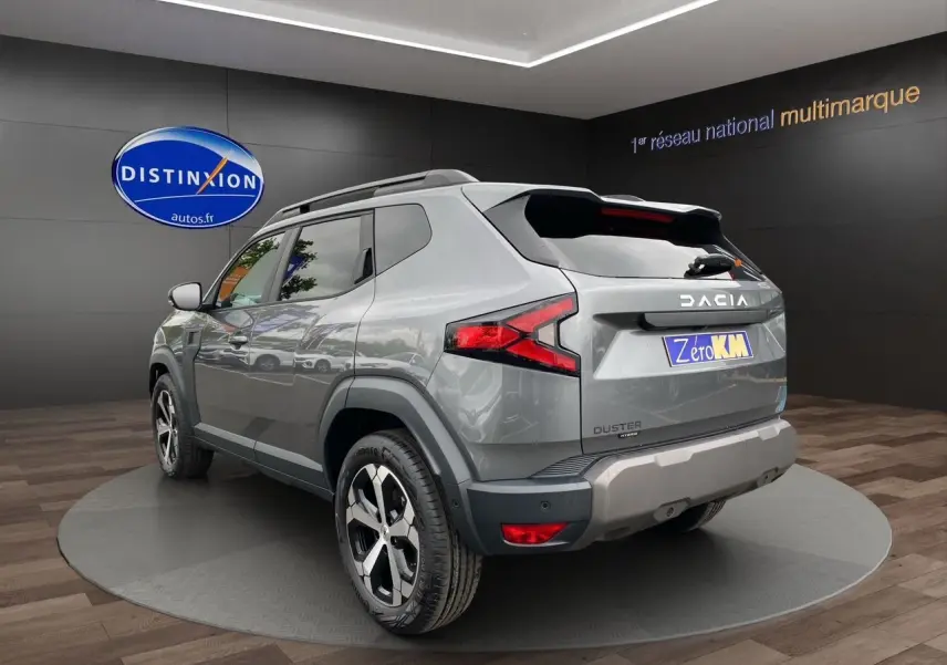 Vue 3/4 arrière droite du Dacia Duster hybride gris schiste avec jantes alliage et feux arrière LED dans un showroom.