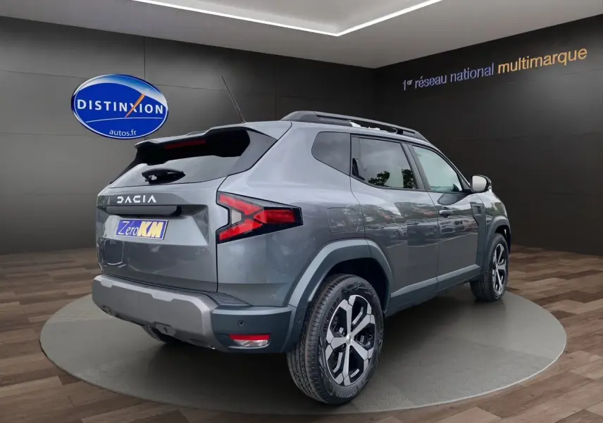 Vue 3/4 arrière droite du Dacia Duster hybride 2025 en gris schiste avec jantes alliage et barres de toit noires.