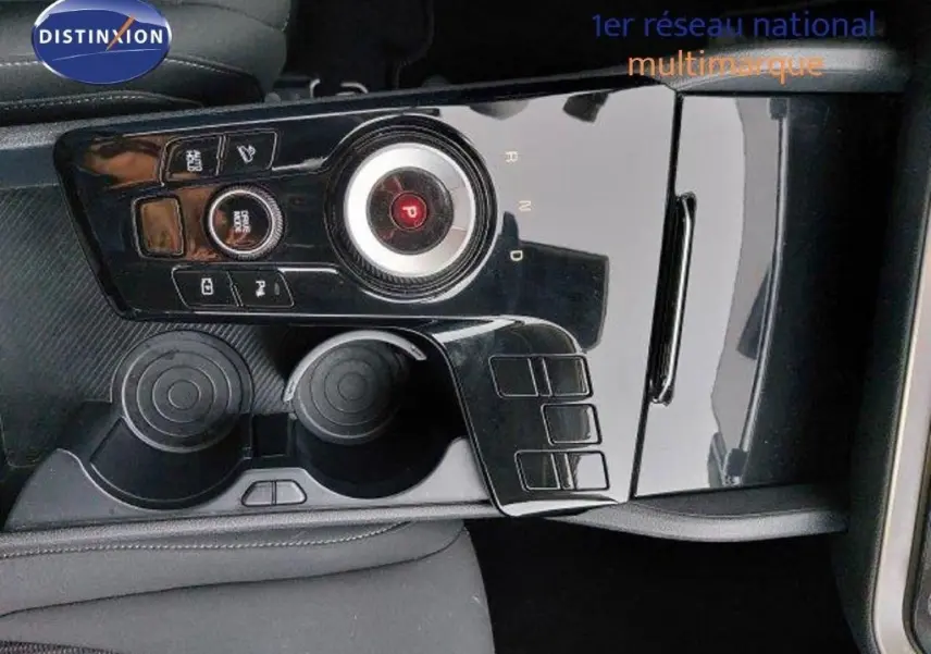 Gros plan sur la console centrale noire brillante du Kia Sportage 2024, avec molette de sélection de vitesse et porte-gobelets.