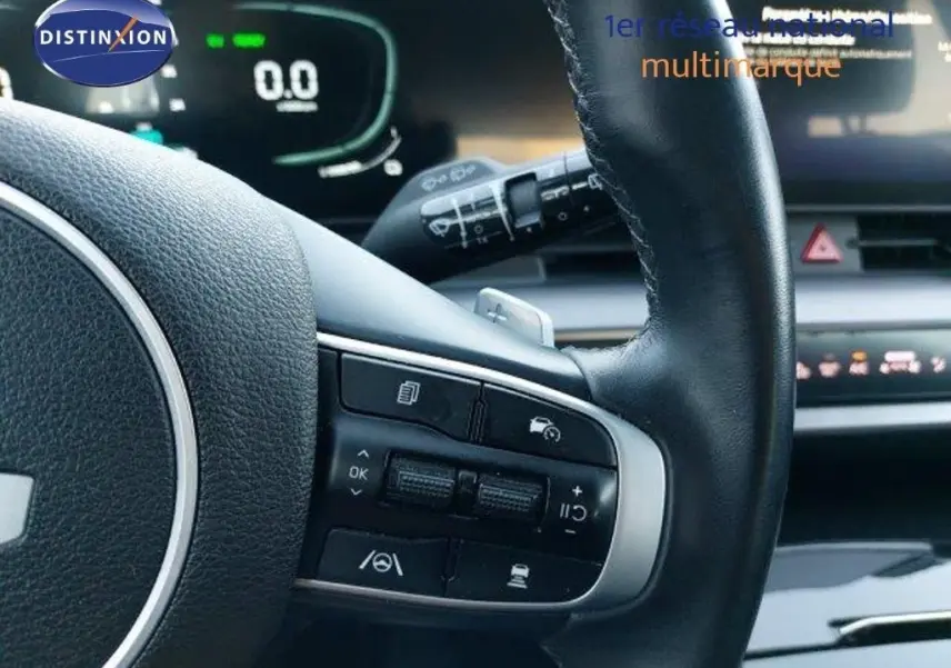 Gros plan sur le volant cuir noir du Kia Sportage 2024 avec commandes intégrées et tableau de bord numérique en arrière-plan.