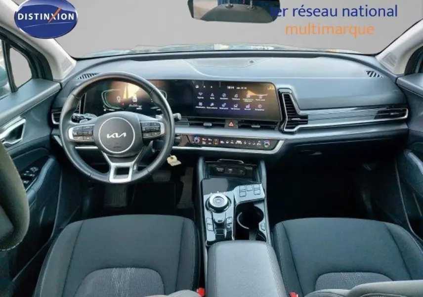 Vue intérieure avant du tableau de bord du Kia Sportage 2024 avec écran tactile large et volant multifonction noir.