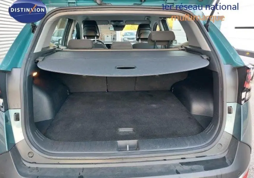 Coffre ouvert vu de l'arrière du Kia Sportage gris Sirius Metal 2024, avec cache-bagages déployé et intérieur spacieux.