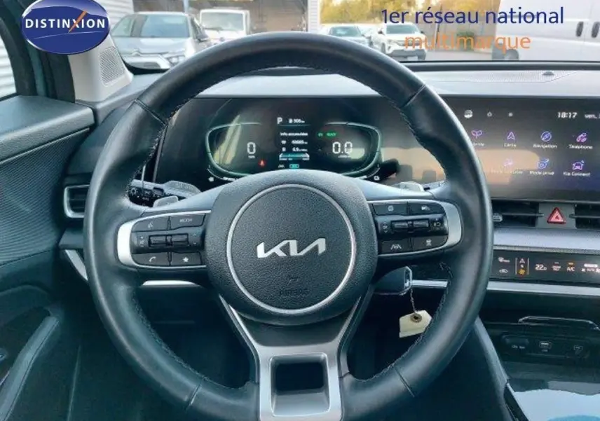 Vue intérieure centrée sur le volant noir du Kia Sportage 2024 avec tableau de bord digital et écran tactile.