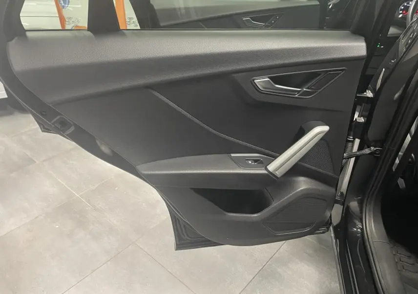 Vue intérieure de la porte arrière gauche noire métallisée de l'Audi Q2 2023 avec poignée et commandes en aluminium.