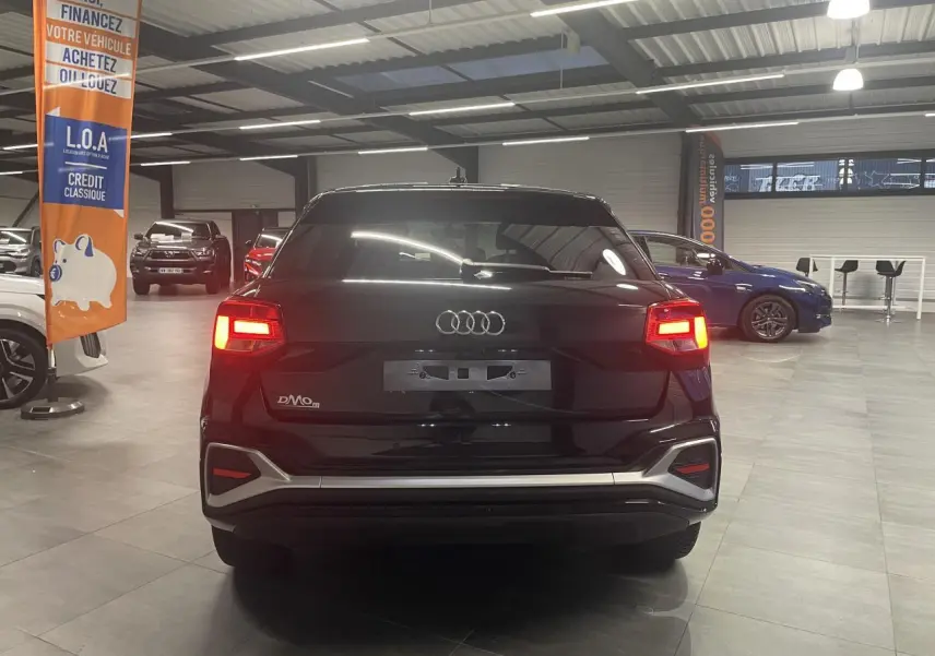 Vue arrière d’un Audi Q2 noir métallisé 2023 avec feux arrière allumés dans un showroom.