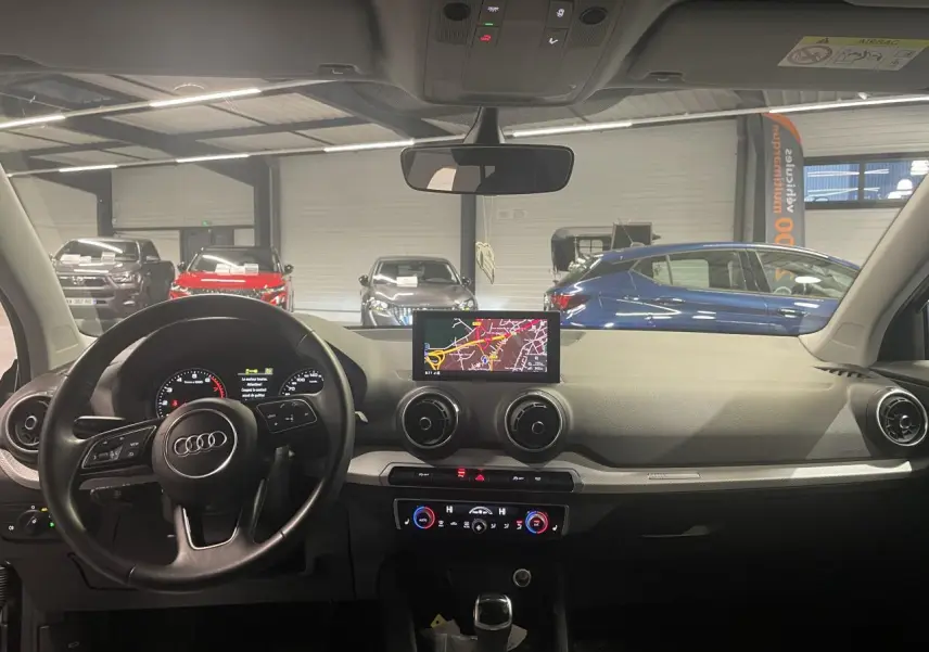 Vue intérieure avant de l'Audi Q2 2023, tableau de bord noir avec écran navigation et volant multifonction S line.