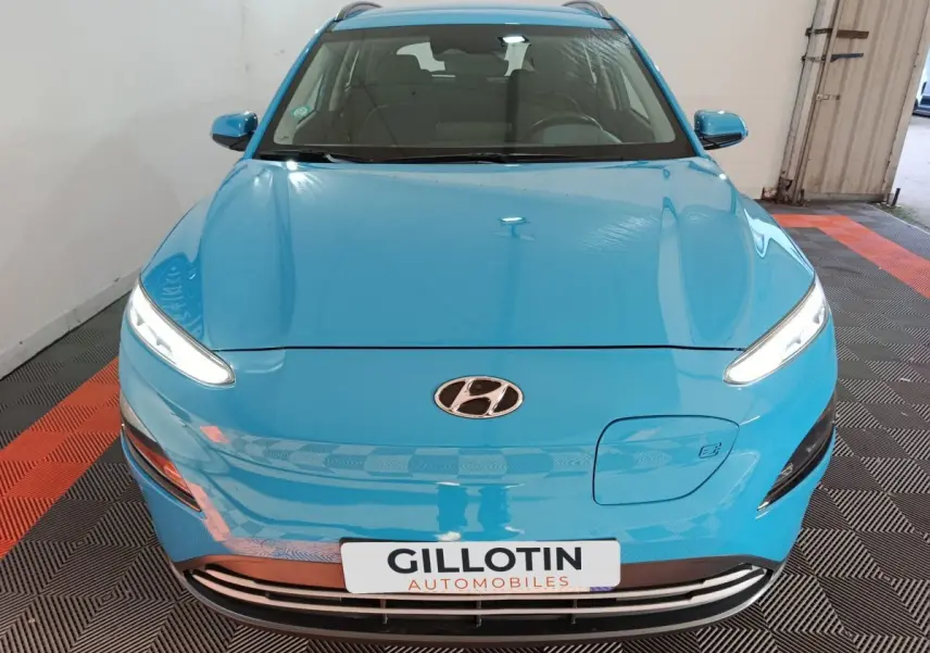 Vue avant d’un Hyundai Kona électrique bleu avec phares LED allumés et logo Hyundai visible sur le capot.