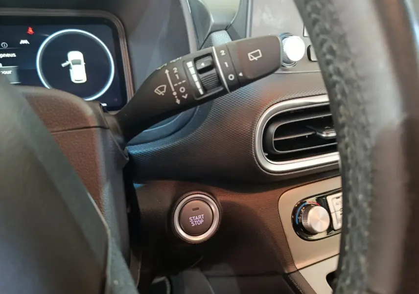 Vue intérieure côté gauche du tableau de bord du Hyundai Kona bleu avec bouton démarrage et commande essuie-glace.