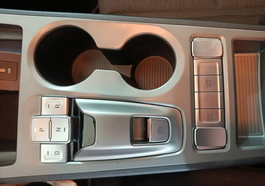 Vue rapprochée de la console centrale grise avec commandes de boîte auto et porte-gobelets du Hyundai Kona électrique bleu 2022.