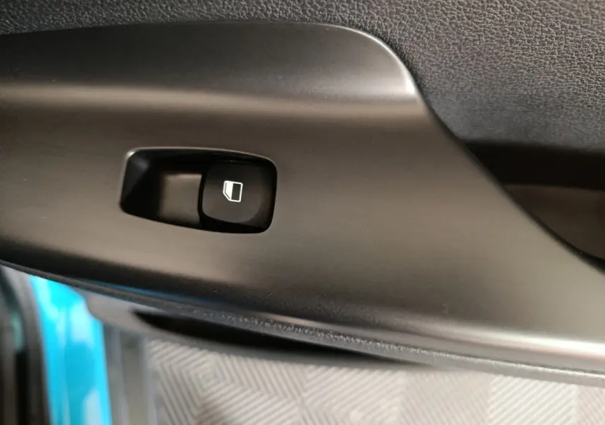 Gros plan sur le bouton de commande de vitre électrique noir dans l’habitacle d’une Hyundai Kona bleu électrique.