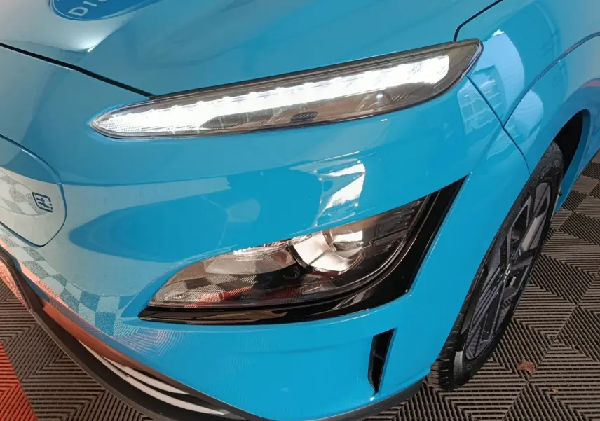 Gros plan sur l'avant droit bleu électrique du Hyundai Kona BEV 64kWh, mettant en valeur les phares LED et la roue.