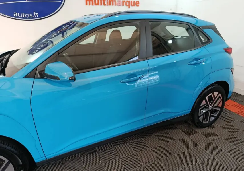 Vue latérale côté gauche d'un Hyundai Kona électrique bleu 2022 avec jantes distinctives et rétroviseur assorti.