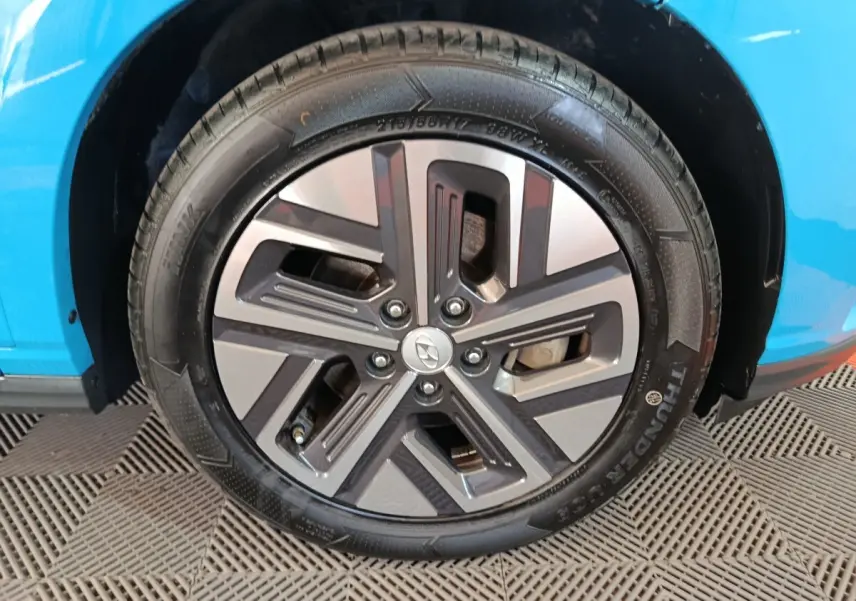 Gros plan sur la roue avant gauche du Hyundai Kona électrique bleu, mettant en valeur la jante au design moderne.