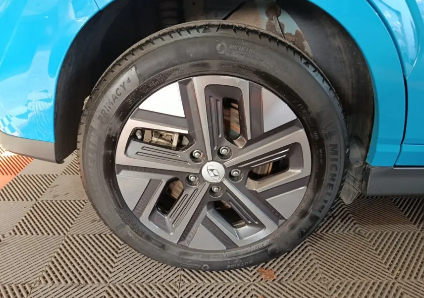 Gros plan sur la roue avant droite d’un Hyundai Kona électrique bleu, avec jante alliage et pneu Michelin.