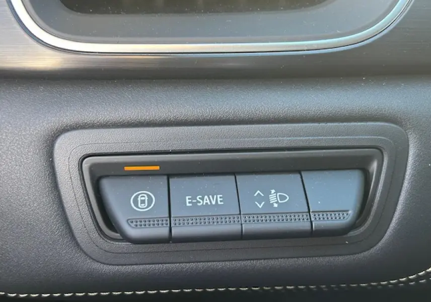 Gros plan sur les boutons de commande noirs du tableau de bord du Renault Symbioz blanc nacré, avec éclairage orange.