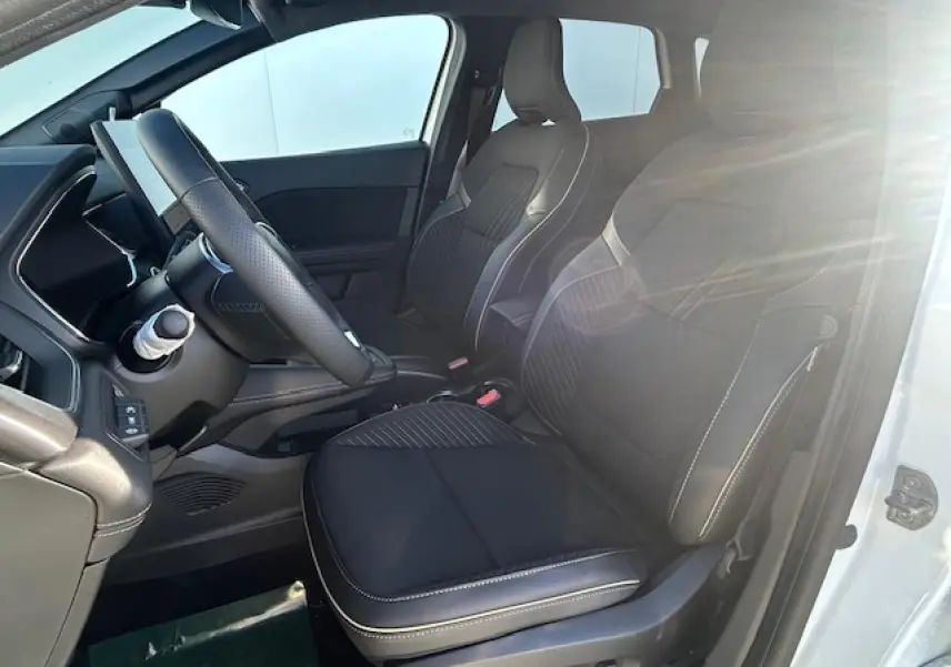 Vue intérieure côté conducteur d'une Renault SYMBIOZ blanc nacré, sièges noirs avec surpiqûres blanches et volant textile.