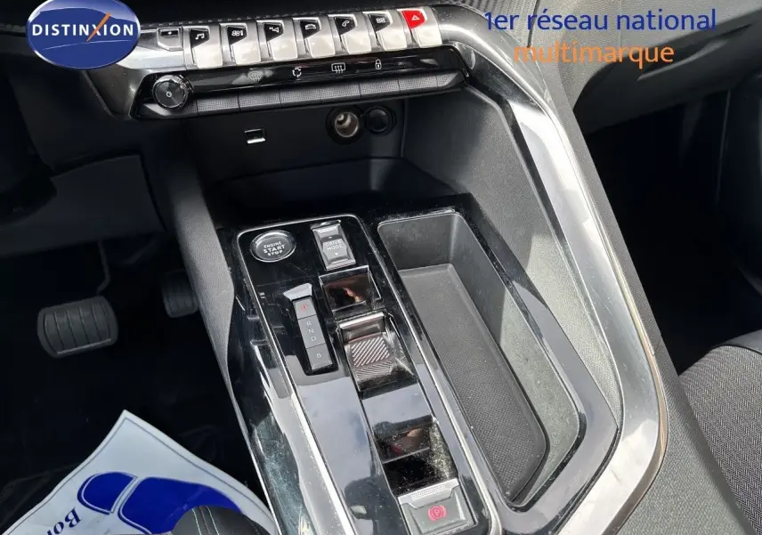 Vue rapprochée de la console centrale noire brillante du Peugeot 3008 Hybrid 2024 avec commandes et rangement.