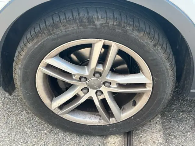 Gros plan sur la roue avant droite d'un Audi Q3 blanc 2015, mettant en valeur la jante alliage à cinq branches doubles.