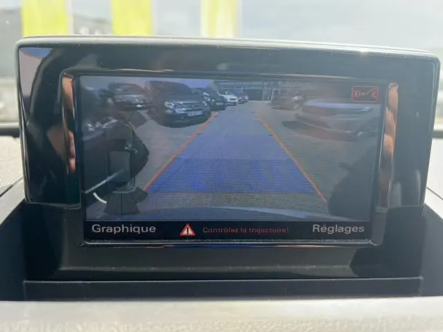 Vue de la caméra de recul de l'Audi Q3 blanc 2015, affichant les lignes de guidage orange et bleues sur l'écran intérieur.