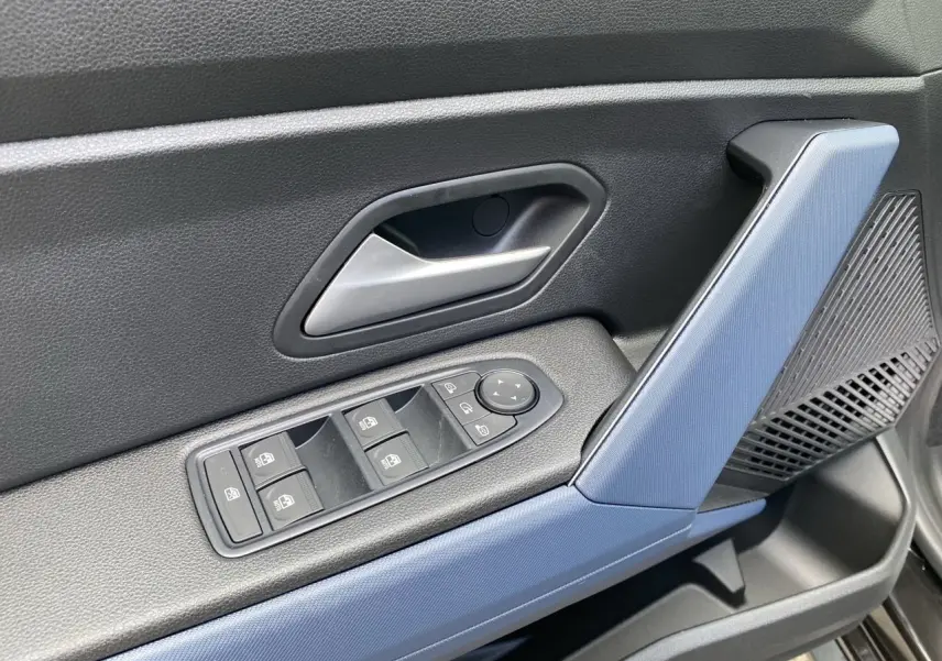 Détail de la porte avant gauche intérieure du Dacia Duster 2025 hybride, avec accoudoir bleu et commandes électriques.