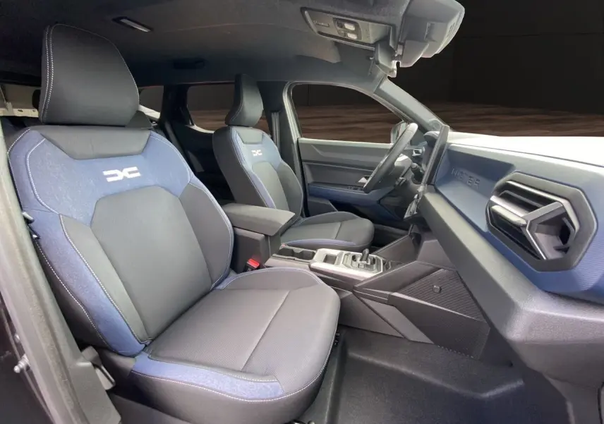 Vue intérieure côté conducteur du Dacia Duster hybride 2025, sièges tissu noir et bleu avec logo DC brodé.