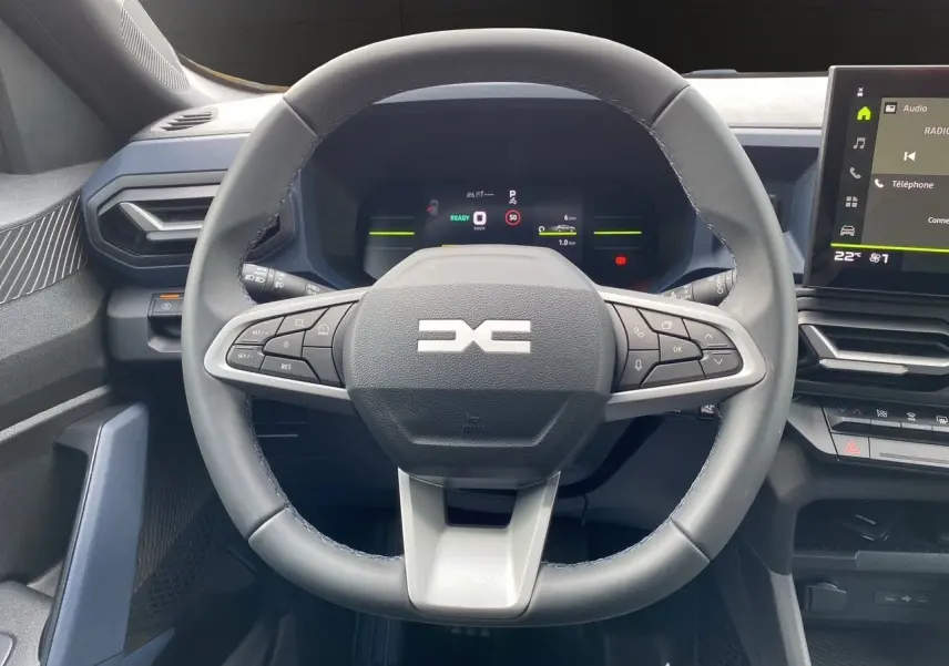 Vue rapprochée du volant noir et gris du Dacia Duster hybride 2025 avec tableau de bord numérique et écran central tactile.