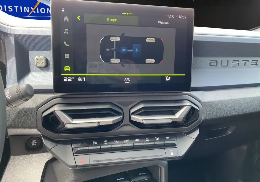 Vue rapprochée du tableau de bord du Dacia Duster hybride 2025, avec écran tactile et aérateurs hexagonaux noirs.