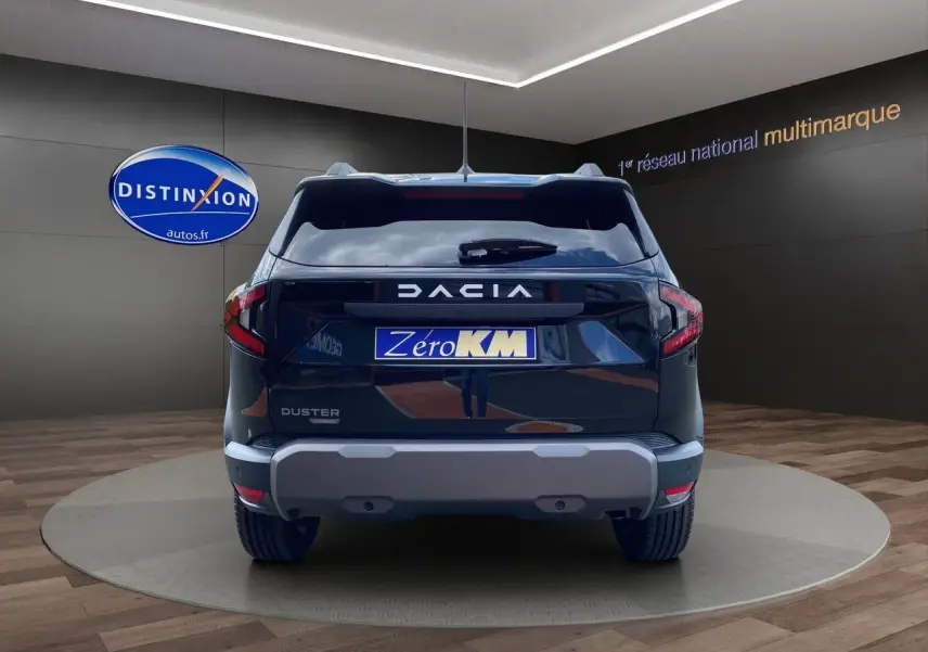 Vue arrière d'un Dacia Duster noir 2025 avec logo et plaque Zéro KM dans un showroom sombre.