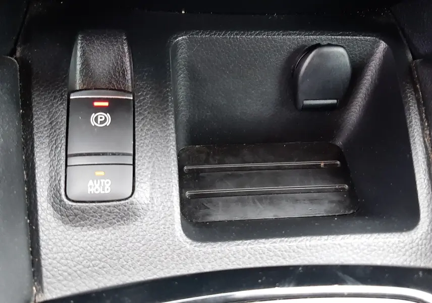 Gros plan sur la console centrale noire du Nissan Qashqai 2020, montrant le frein à main électrique et un espace de rangement.
