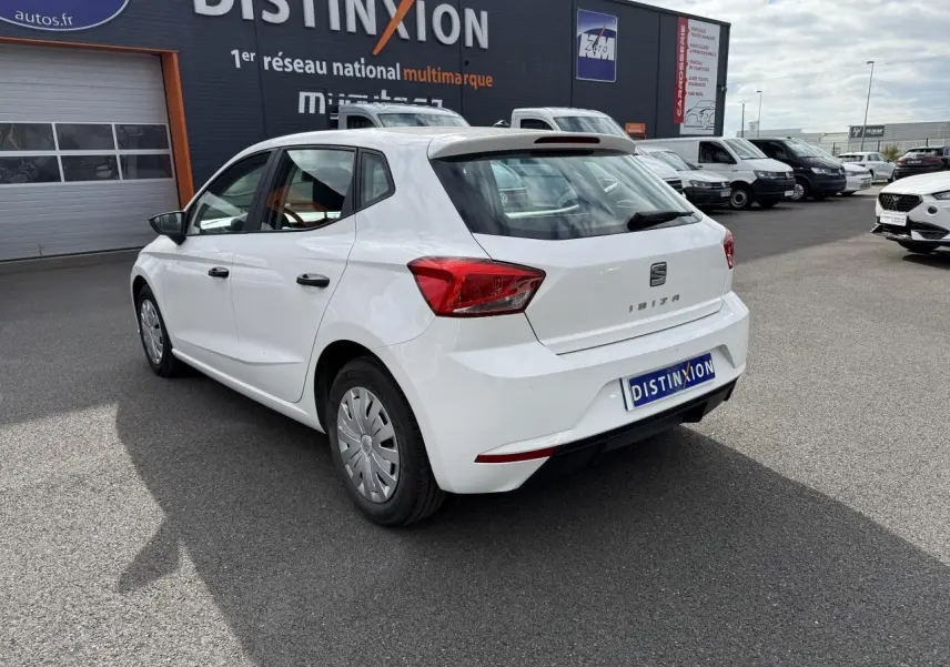 Vue 3/4 arrière droite d'une SEAT Ibiza blanche Candy 2019 avec jantes enjoliveurs et feux arrière distinctifs.