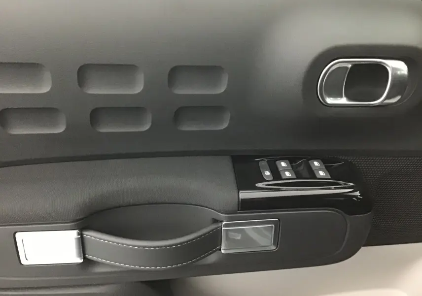 Gros plan sur la poignée intérieure côté gauche de la porte d'une Citroën C3 2022 gris platinium/noir avec commandes de vitres.