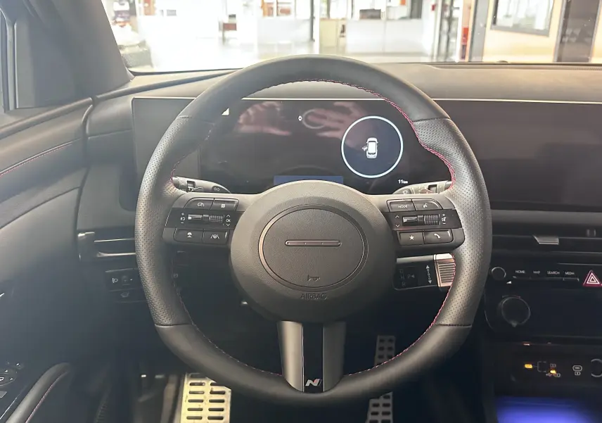 Vue intérieure du tableau de bord du Hyundai Tucson 2025 hybride, avec écran tactile affichant l'usage moteur et éclairage d'ambiance bleu.