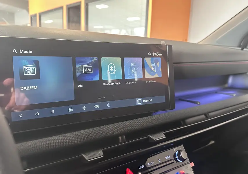 Vue intérieure du tableau de bord du Hyundai Tucson 2025, écran tactile large avec ambiance lumineuse bleue et surpiqûres rouges.