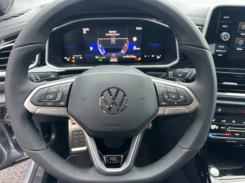 Vue rapprochée du volant cuir multifonction noir du Volkswagen T-Roc gris avec tableau de bord numérique et écran tactile.