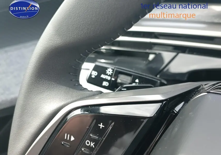 Gros plan sur les commandes multifonctions noires du volant cuir d’une Peugeot 3008 bleu, intérieur moderne.