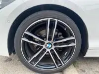 Gros plan sur la roue avant droite noire et argentée d'une BMW Série 1 blanche 114d M Sport de 2018.
