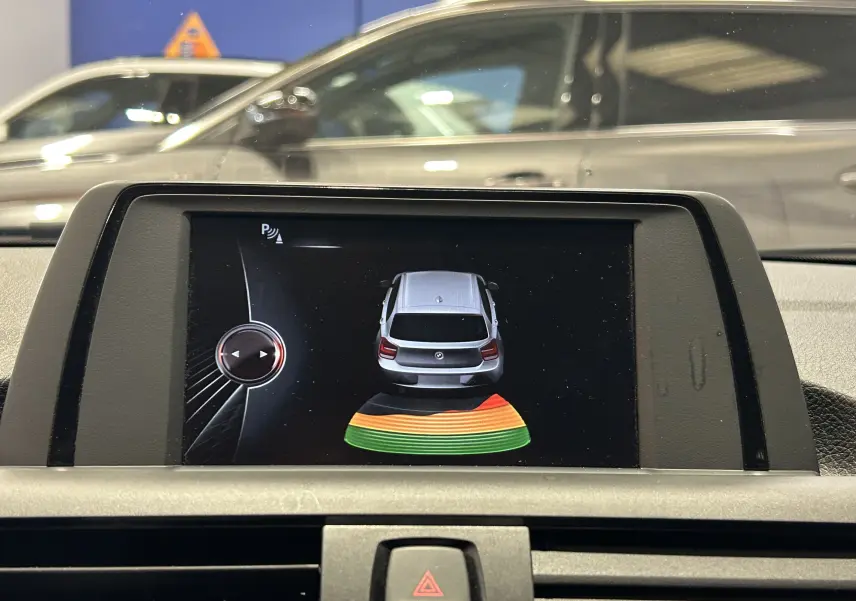Écran de la BMW Série 1 16d gris montrant l'alerte radar de recul avec visualisation arrière colorée.